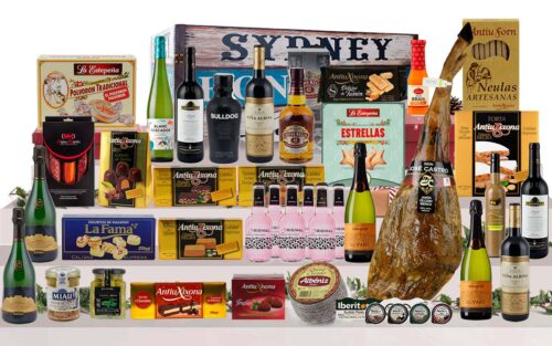 Baúl gourmet amb pernil ibèric de cebo de Salamanca, Corpinnat, caves, vins de Rioja, vi blanc, licors, whisky, ginebra, tòniques, ibèrics, formatge, torrons, bombons i una gran selecció de dolços, presentat en un baúl de fusta pintat.